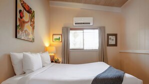 A hotel room with a large bed, an air conditioning unit, a window with curtains, and artwork on the walls.