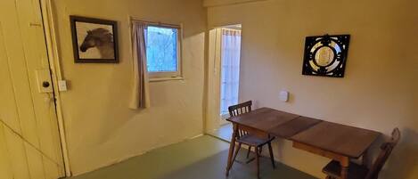A room with a wooden dining table and chairs, a framed picture on the wall, a window with curtains, and a ceiling light fixture.