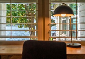 Ein Zimmer mit Blick auf das Wasser, durchzogen von Jalousien, mit einem Tisch und einer Lampe.