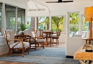 A sunlit room with a large window, a ceiling fan, wicker furniture, and a white sofa. - Historic Lakefront Cottage with Dock & Patio (Hot Springs)