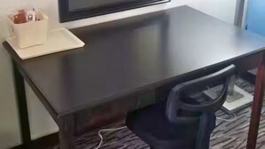 A hotel room with a dark wooden desk, a chair, a mirror, and a small table with a tissue box. - OSU 223 Queen Bed Hotel Room (Stillwater)