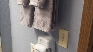 A bathroom with a towel rack holding two towels, a hairdryer plugged in, and toiletries on the counter. - OSU 223 Queen Bed Hotel Room (Stillwater)