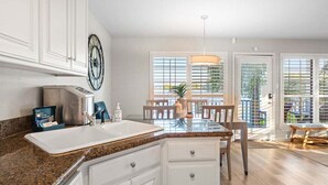 Cocina con encimera de granito, armarios blancos, pileta de acero inoxidable y comedor con mesa y sillas.