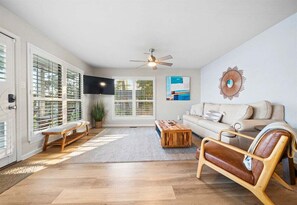 A living room with a sofa, a wooden bench, a coffee table, a ceiling fan, and a TV mounted on the wall. - Waterfront Getaway with Deck & Boat Slip (Hot Springs)