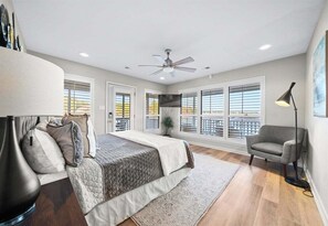 A bedroom with a bed, a chair, a floor lamp, a ceiling fan, and large windows. - Waterfront Getaway with Deck & Boat Slip (Hot Springs)