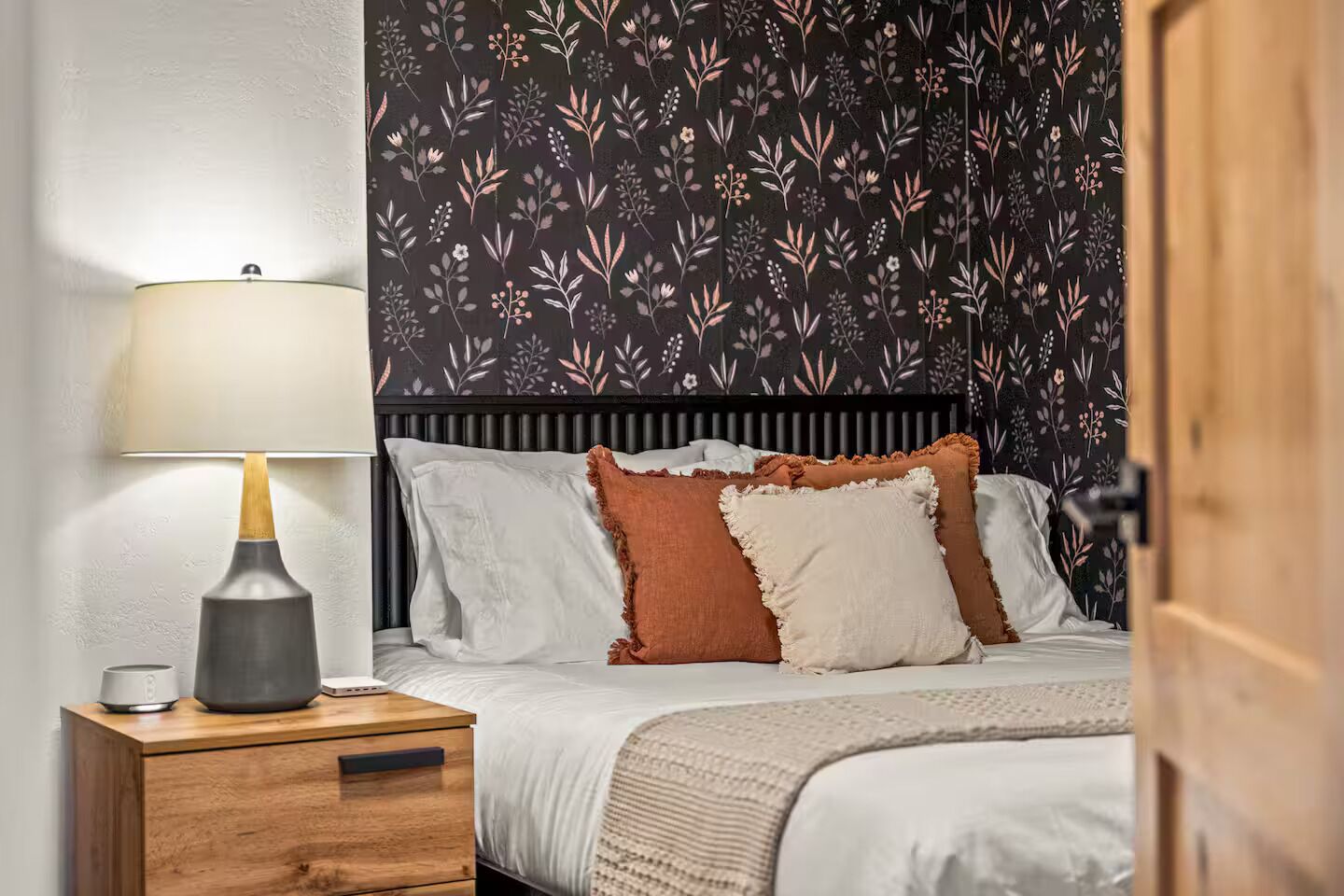 A bedroom with a bed, pillows, a bedside table with a lamp, and a nightstand.
