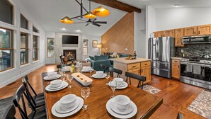 A modern kitchen with stainless steel appliances, a dining area with a wooden table set for a meal, and a cozy living space with a fireplace. - Mountain View Retreat - Game Room + 2 Living Areas (Black Hawk)