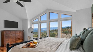 A bedroom with a large bed, a wooden dresser, a ceiling fan, and a view of a mountainous landscape through large windows. - Mountain View Retreat - Game Room + 2 Living Areas (Black Hawk)