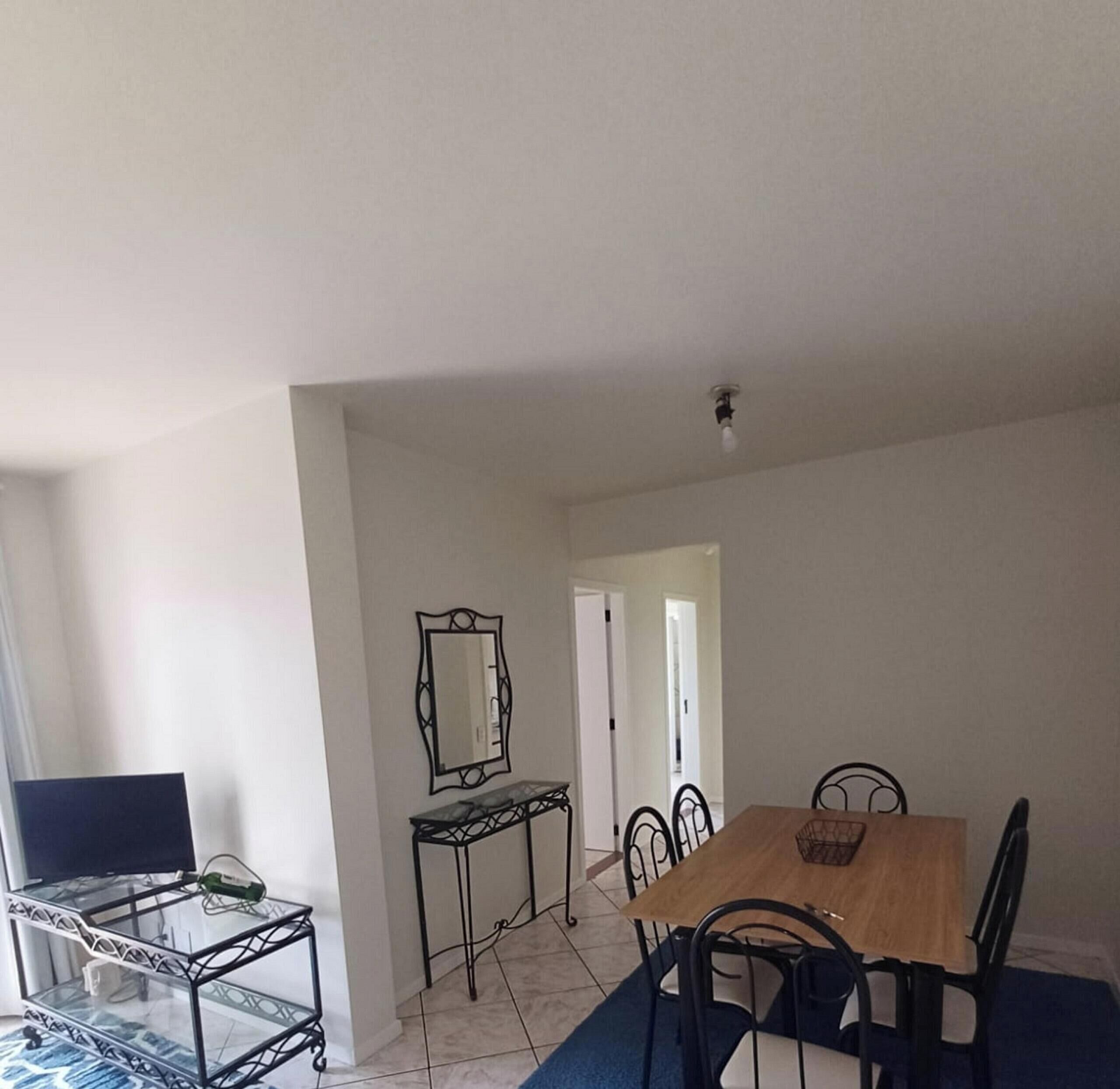 Un comedor con una mesa de madera, sillas negras, una mesa con cubierta de vidrio y una botella, y un espejo en la pared.