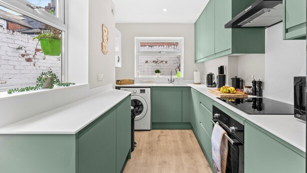 A compact kitchen with green cabinets, a washing machine, and a window with plants. - Modern | Chester Retreat | Free Parking | Sleeps 6 | (Chester)