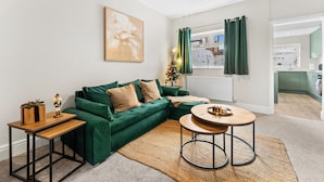 A modern living room with a green sofa, a wooden coffee table, and a small side table with a plant. - Modern | Chester Retreat | Free Parking | Sleeps 6 | (Chester)