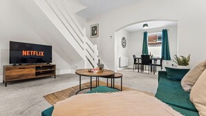 A modern living room with a TV, sofa, coffee table, and staircase. - Modern | Chester Retreat | Free Parking | Sleeps 6 | (Chester)