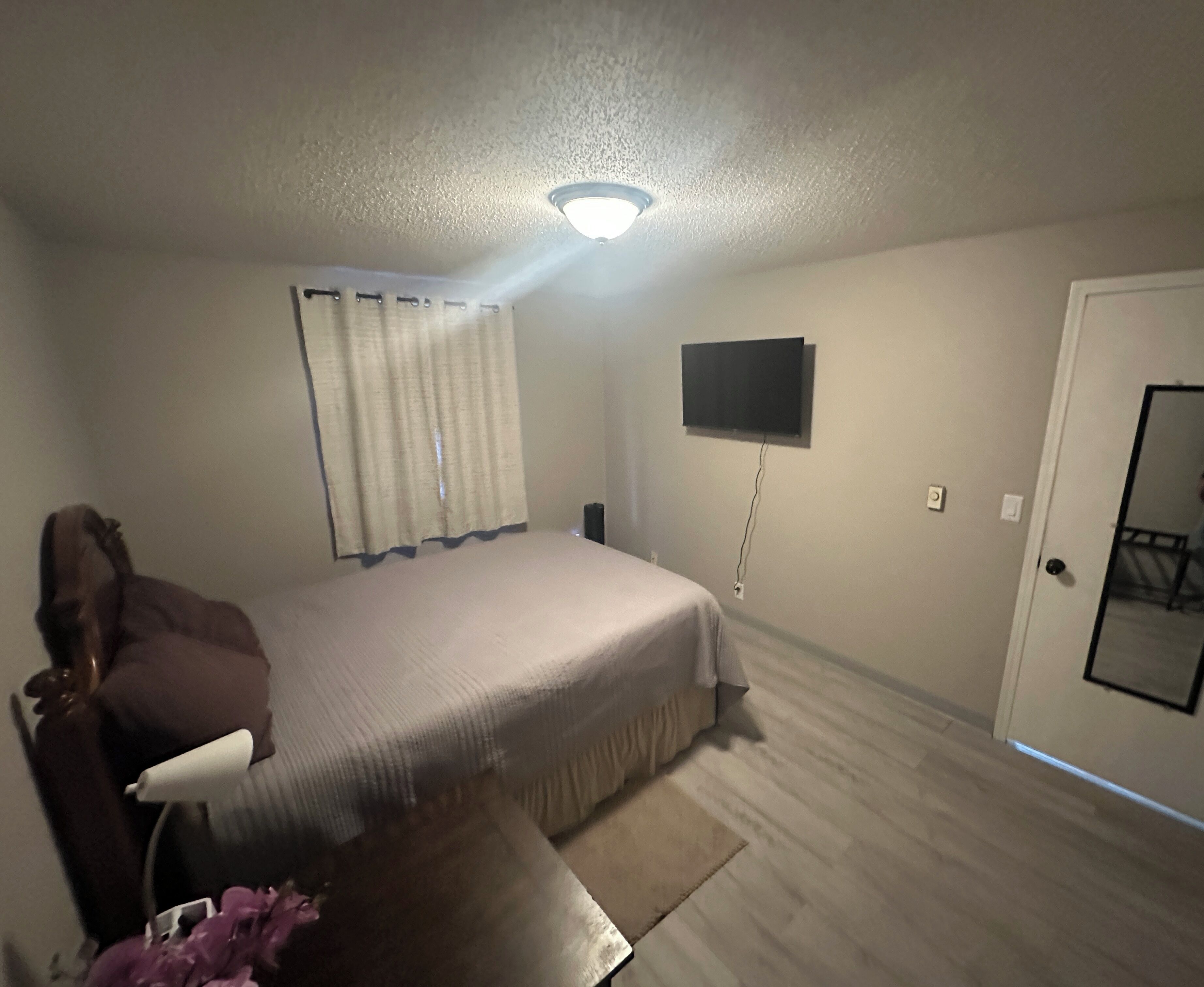 A bedroom with a bed, a TV mounted on the wall, a door, and a ceiling light.