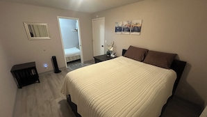 Un dormitorio con una cama grande, una mesita de noche, una silla, un espejo y una puerta que da a otra habitación.