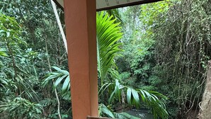 A wooden table and chair set on a balcony with a view of dense greenery and a water body. - Lovely 1-bedroom private bungalows at riverside resort with AC and full kitchen. (ตำบล เกาะลันตาใหญ่)