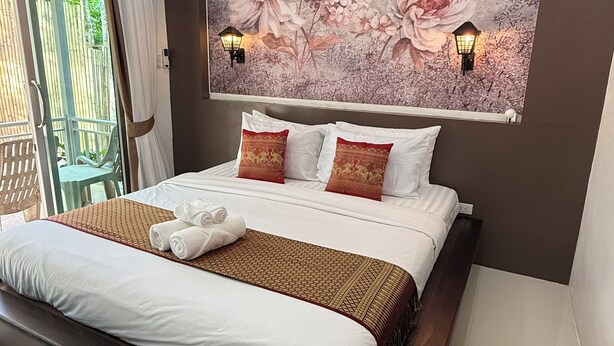 A modern hotel room with a large bed, a decorative floral wall mural, two wall-mounted lamps, and a view of the outdoors through a sliding door. - Lovely 1-bedroom private bungalows at riverside resort with AC and full kitchen. (ตำบล เกาะลันตาใหญ่)
