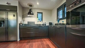 A modern kitchen with stainless steel appliances, wooden flooring, and a pendant light. - Maison piscine proche Alpilles (Noves)