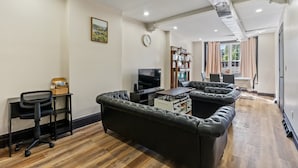 A modern living room with a black leather sofa, a TV, and a dining area with a table and chairs. - Spacious Home In Troy (Troy)