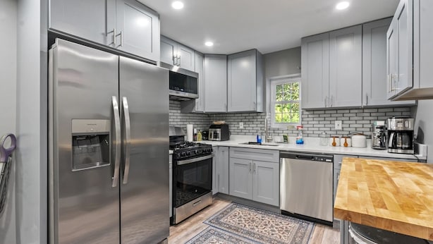 A modern kitchen with grey cabinets, stainless steel appliances, and a wooden countertop. - Spacious Home In Troy (Troy)