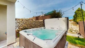 Jacuzzi al pati d'una casa amb mur de pedra, llums de cadena i zona enjardinada.