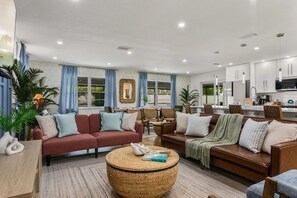 A modern living room with sofas, a round coffee table, and a kitchen area visible through the glass doors. - Tropic Luxe - Saltwater Pool + Hot Tub + 3 Miles to IMG (Bradenton)