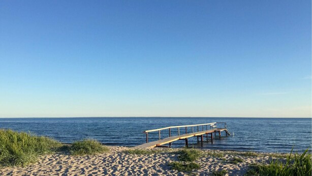 Ein Strand mit einer hölzernen Seebrücke, die sich ins Meer erstreckt.