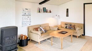 Ein gemütliches Wohnzimmer mit einer Sofagarnitur, einem Holztisch, einem schwarzen Herd und einer Wand mit einem Poster.