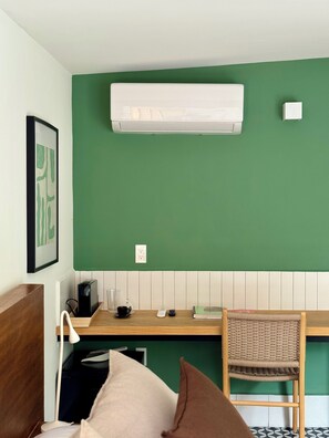 A room with a green wall, a white air conditioner, a wooden desk, a wicker chair, and a framed picture. - oolena Unique Studio w/private terrace (Ciudad de México)