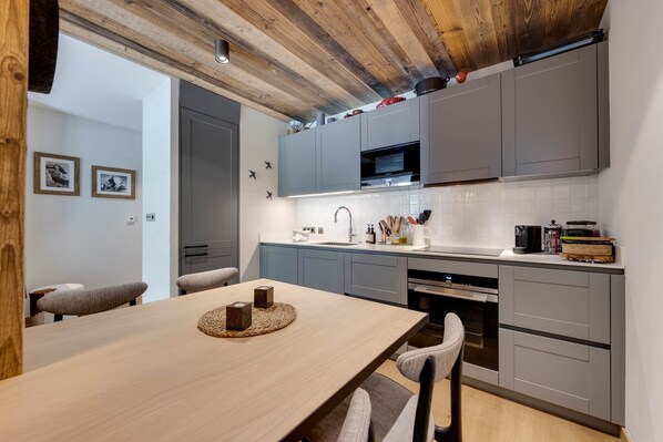 A modern kitchen with grey cabinets, a wooden ceiling, and a dining area with a table and chairs. - Lièvre Blanc - Last In The Valley (Val-d'Isère)
