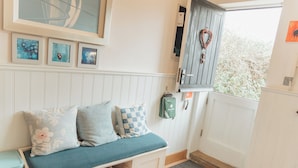 A cozy room with a bench, framed artwork, a basket, and a view of greenery outside. - Bull Pen Cottage | A Luxury Cosy Countryside Retreat (Beaconsfield)