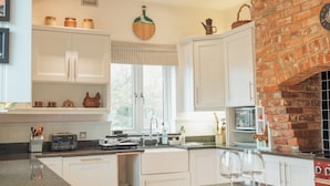 A modern kitchen with white cabinets, a brick oven, and a large island with bar stools. - Bull Pen Cottage | A Luxury Cosy Countryside Retreat (Beaconsfield)