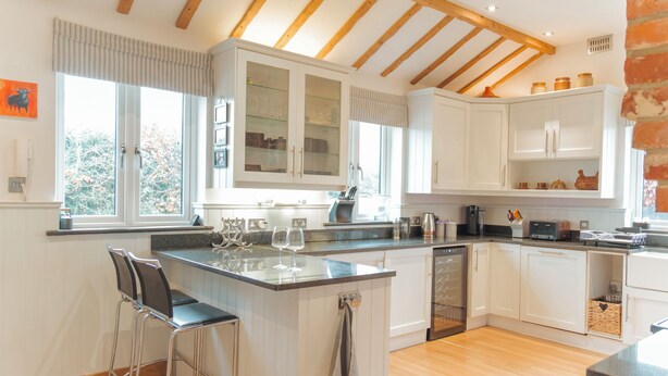 A modern kitchen with white cabinetry, a central island with bar stools, and a wooden ceiling. - Bull Pen Cottage | A Luxury Cosy Countryside Retreat (Beaconsfield)
