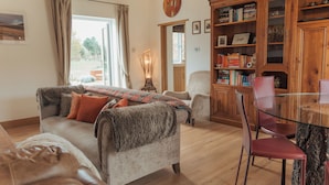 A cozy living room with a sofa, armchairs, a glass coffee table, and a wooden bookshelf. - Bull Pen Cottage | A Luxury Cosy Countryside Retreat (Beaconsfield)