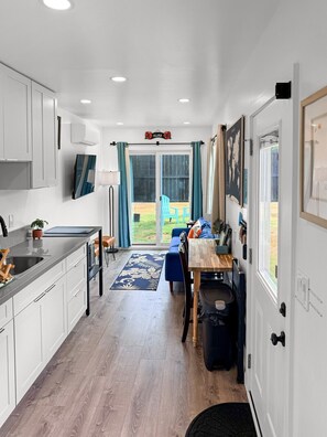 A modern kitchen with white cabinets, a wooden dining table, and a view to a backyard. - Hibiscus Hale - Perfect for 2! (Waialua)