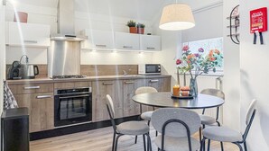 Une cuisine moderne avec des meubles en bois, un four encastré et un coin repas comprenant une table ronde et des chaises grises.