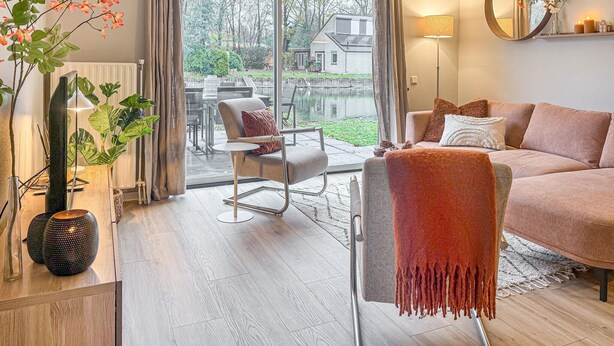 Un salon moderne avec un canapé, un fauteuil et une vue sur une maison, visible à travers de grandes fenêtres.