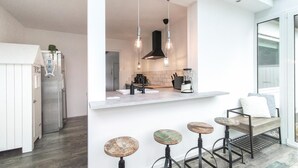 A modern kitchen with a central island, bar stools, pendant lighting, and a view of the adjacent living area.