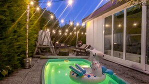 An outdoor swimming pool with inflatable toys, surrounded by lounge chairs and a deck.