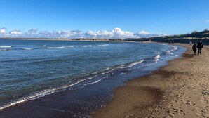 A beach with waves, a clear sky, and people walking.