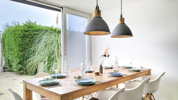 A dining area with a wooden table set for four, white chairs, and two hanging pendant lights.
