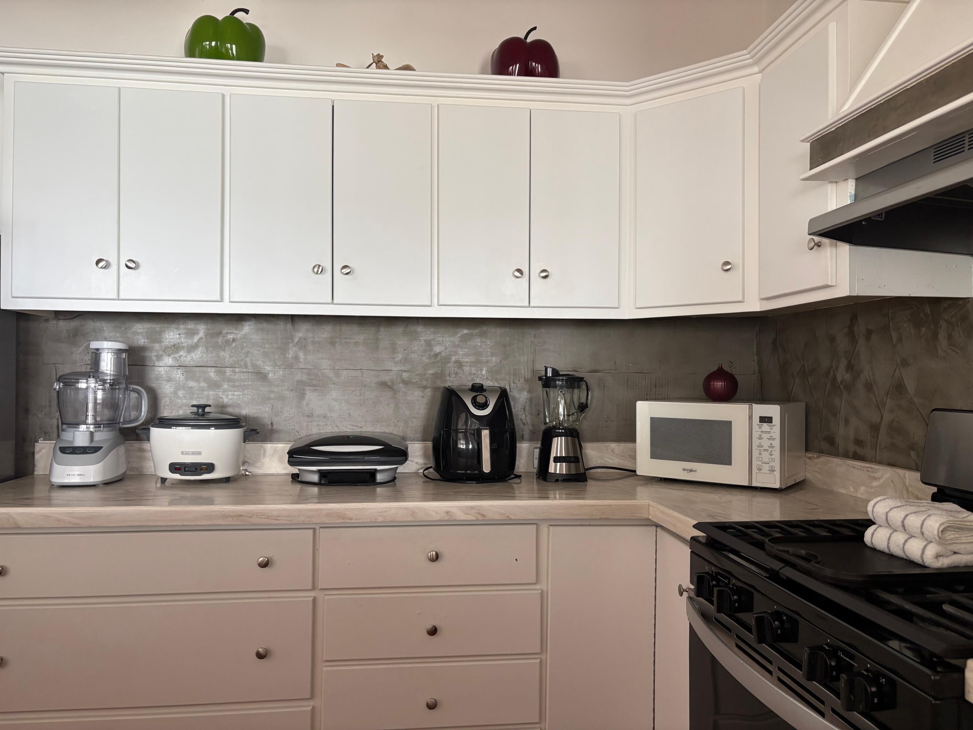 A kitchen with white cabinets, a stove, a microwave, a blender, a coffee maker, and a slow cooker.