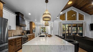 A modern kitchen with a large island, stainless steel appliances, and a unique hanging light fixture. - Lake-View Gem w/ Outdoor Entertainment in Show Low (Show Low)