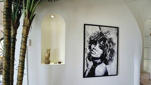 Un mur orné d’un portrait en noir et blanc encadré, une petite étagère sur laquelle repose une statue et une grande plante.