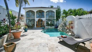 Ein modernes Haus mit Swimmingpool, umgeben von Topfpflanzen und Palmen.