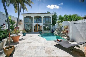 Ein modernes Haus mit Swimmingpool, umgeben von Topfpflanzen und Palmen.