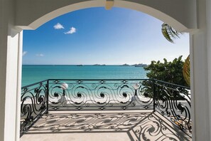 Ein Balkon mit aufwendiger Metallverzierung, der auf ein türkisblaues Meer und ferne Inseln blickt.