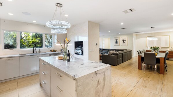 A modern kitchen with a marble island, a built-in oven, and a dining area with a wooden table and chairs. - LA Hillside Retreat w/ Pool, Views, Fire Pit & Outdoor Lounging Casa Bellagio by Avantstay (Los Angeles)