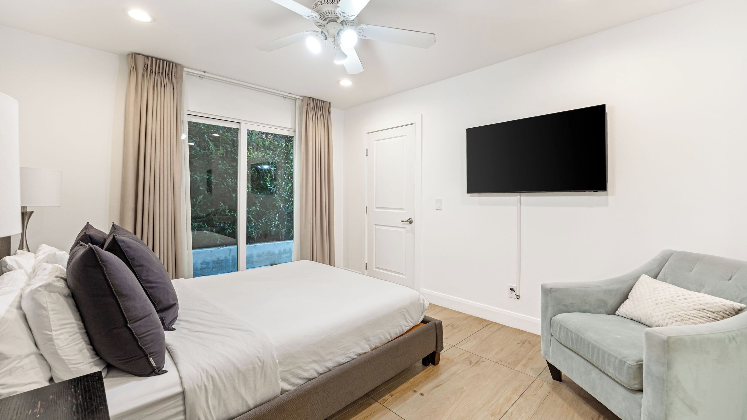 A bedroom with a bed, a chair, a TV, and a sliding glass door.