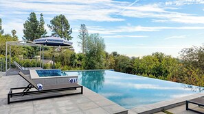 Ein Swimmingpool mit Sonnenschirm, Liegestühlen und Blick auf Bäume und Gebäude.