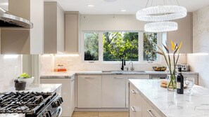 A modern kitchen with a central island, a gas stove, a double sink, and a large window with a view of greenery. - LA Hillside Retreat w/ Pool, Views, Fire Pit & Outdoor Lounging Casa Bellagio by Avantstay (Los Angeles)